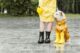 Person wearing yellow raincoat with black rain boots next to white dog wearing yellow raincoat and yellow rain boots outside